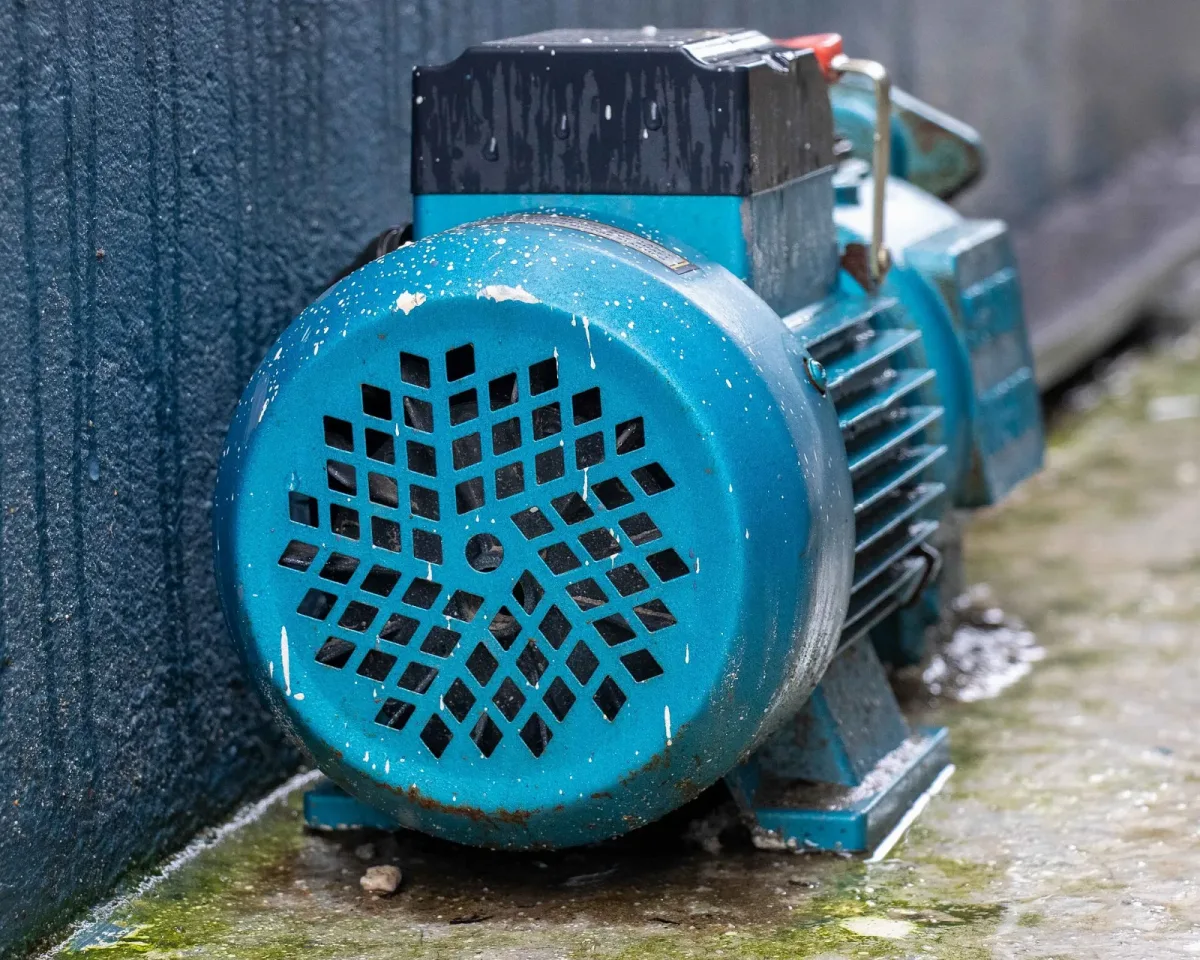 Pompa electrica albastra de apa asezata langa un perete, cu motor si carcasa ventilata