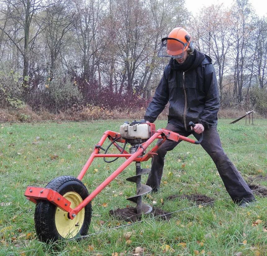 Om cu casca si viziera manevreaza un motoburghiu pe roata care sapa o groapa in iarba